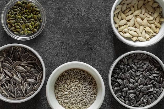 Sunflower black and pumpkin seeds in bowls on grey tablecloth on dark background top view