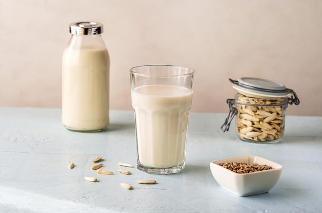 Sunflower milk in a glass and bottle raw seeds in jar and bowl on light blue background