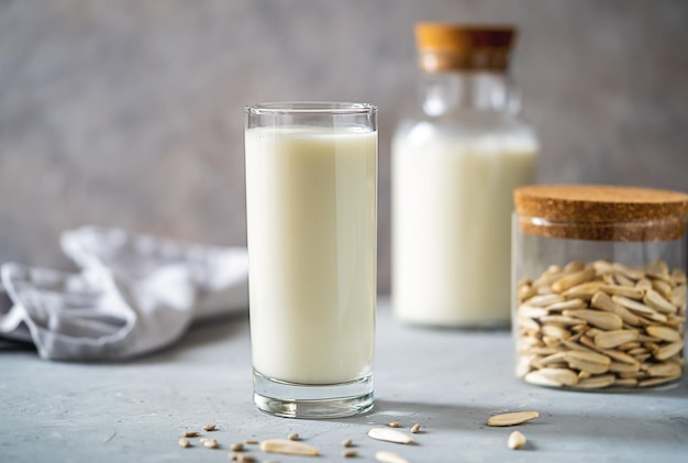 Sunflower milk in a glass and bottle raw seeds in jar napkin on concrete background