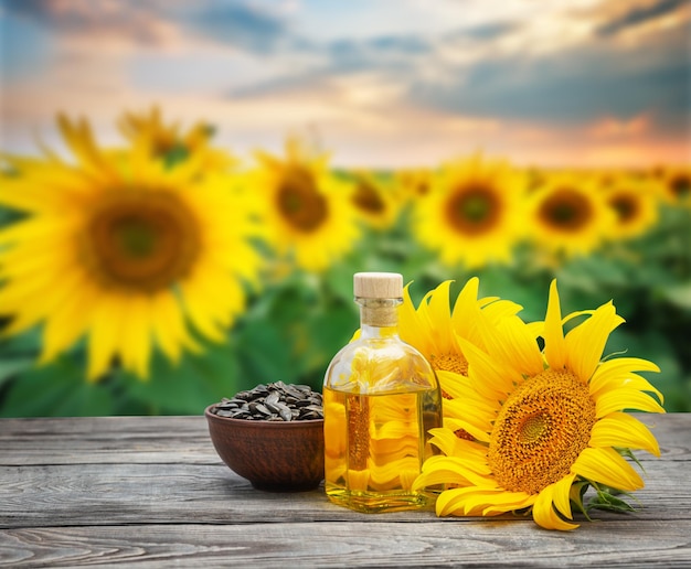 Foto olio di girasole in bottiglia e semi con fiori di girasole sullo sfondo di un campo di girasoli al tramonto