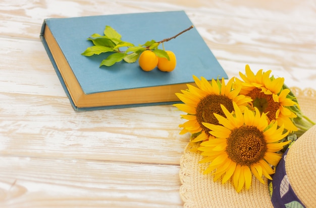 Sunflower, straw hat, book and yellow plum on table