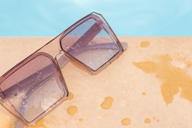 sunglasses against the cloudy sky or on edge of the pool,blue water in background.water drops