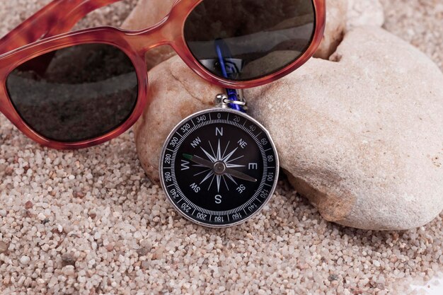 Sunglasses and a compass on a stone in the sand closeup