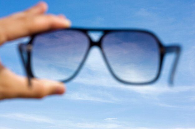 Sunglasses in hands of man with sky view