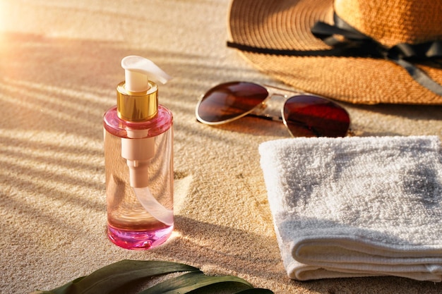 Солнцезащитные очки возле соломенной шляпы и бутылка с маслом для загара на песчаном пляжном полотенце и тени от пальмовых листьев