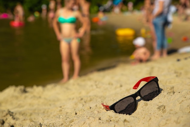 Sunglasses in sand at beach blurred people on background summe