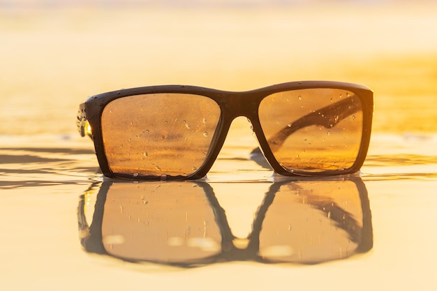 Sunglasses on sand beautiful summer beach and golden light of sunset