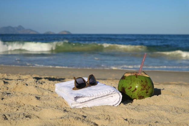 Sunglasses, towel and a fresh young coconut on the sandy beach, Copacabana, Rio de Janeiro, Brazil