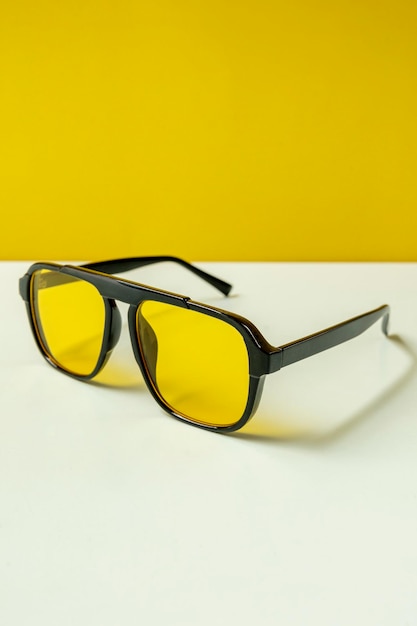 Солнцезащитные очки с черной оправой и желтыми линзами на гладкой голубой поверхности