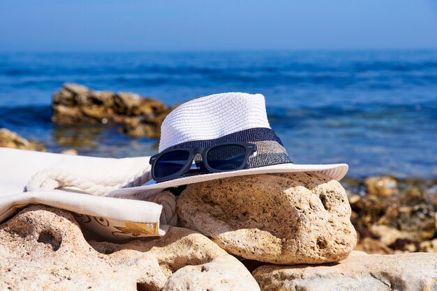 Sunglasses with a hat and a beach bag  on a stone on the background of the sea.