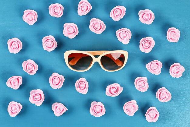 Sunglasses with little roses on blue background. Top view. Summer background. Flat lay.