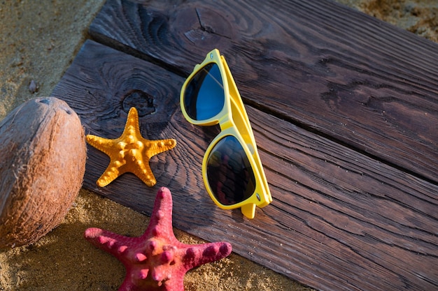 Photo sunglasses with yellow frames lie on the beach next to starfish and coconut