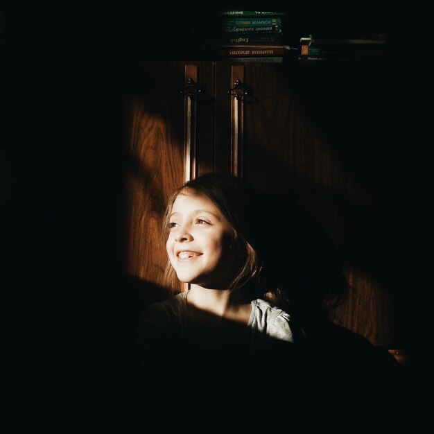 Фото Солнечный свет падает на улыбающуюся девушку, стоящую дома.