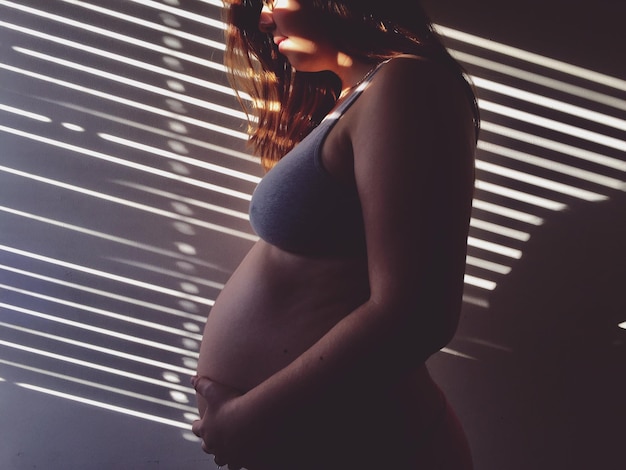 Photo sunlight falling on pregnant woman standing by wall