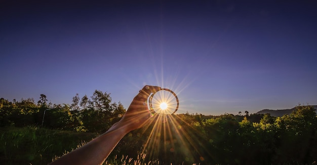 Photo sunlight streaming through glass held by person against sky