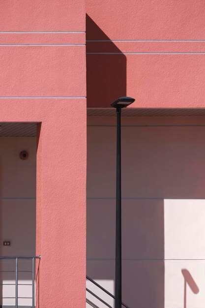 Sunlight on surface of black LED street lamp post beside entrance way of pink office building