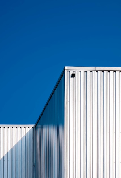 Sunlight on surface of corrugated steel wall of warehouse building against blue clear sky