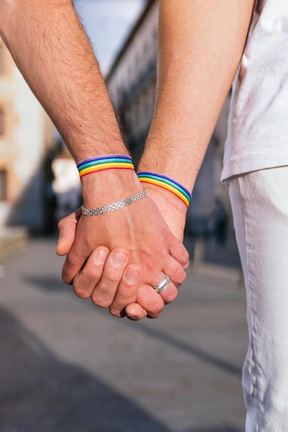 Foto passeggiata in città illuminata dal sole mani irriconoscibili che si stringono indossano braccialetti arcobaleno in mezzo a un vivace orgoglio lgbt