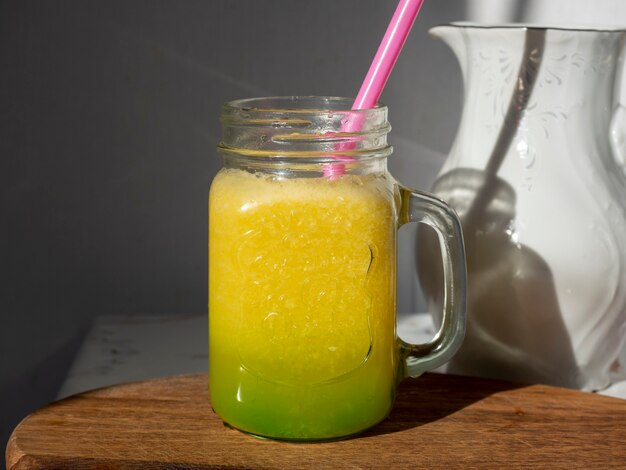 Sunlit glass jar with yellow smoothies. There's a drinking tube in the jar.