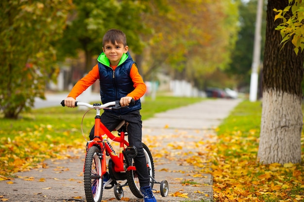 晴れた秋の日。都市公園で自転車に乗っている少年。リラクゼーションと楽しい娯楽のコンセプト。サイドスペースが空の写真。