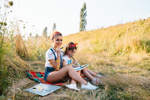 Sunny nature, mom and daughter paint a picture in a park , painting a Little Child, Child Creativity. 