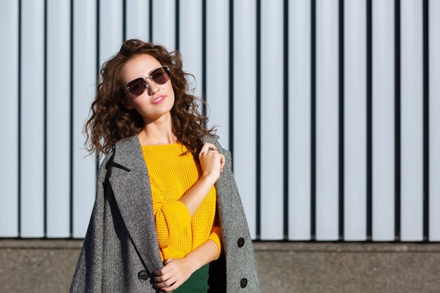 Sunny portrait of lovely hipster girl walking down the street, posing near the shutters. Space for text