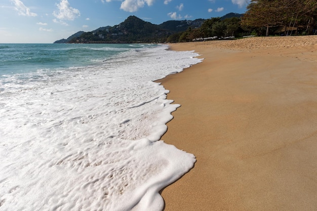 Sunny sandy beach and foam from waves crashing on shore with mountains in background Samui Thailand