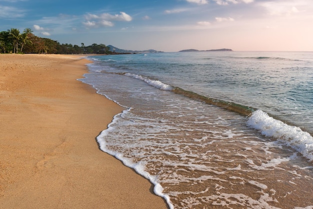 Sunny sandy beach and foam from waves crashing on shore with mountains in background Samui Thailand