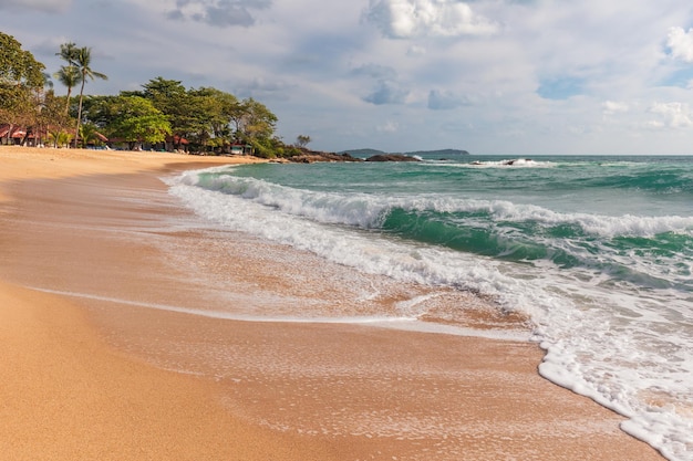 Sunny sandy beach and foam from waves crashing on shore with mountains in background Samui Thailand