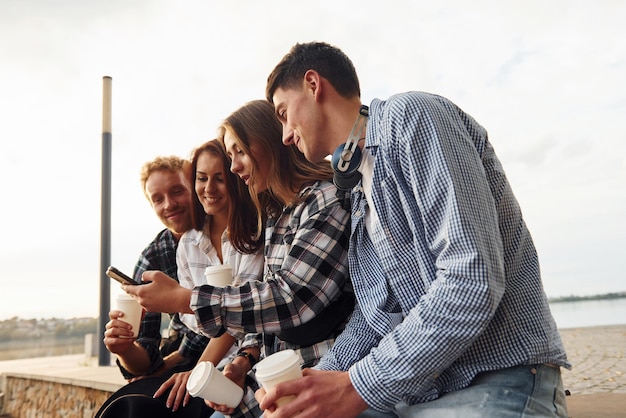 Sunny weather drinking coffee group of young cheerful friends
that is outdoors having fun together