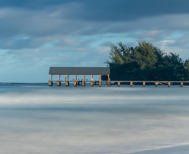 Sunrise lights the dawn sky above Hanalei Pier with long duration exposure to blur waves near Hanalei Kauai Hawaii