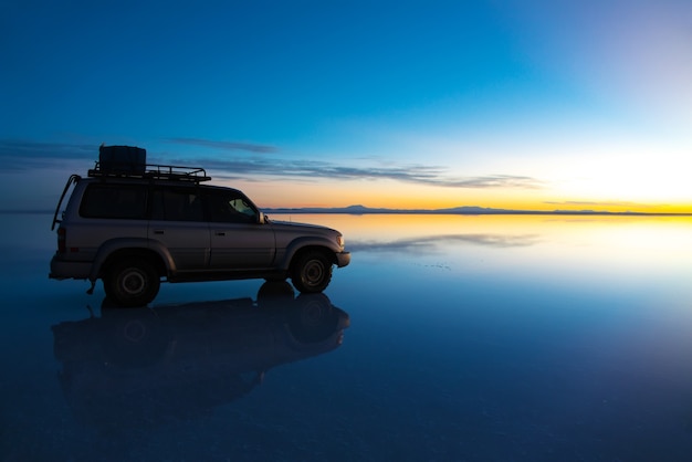 볼리비아의 Salar de Uyuni 일출은 물, 소금 평평한 사막과 하늘 반사의 자동차로 덮여 있습니다.