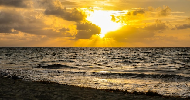 Sunrise or a sunset above the sea taken from a sandy beach partially hidden by the clouds