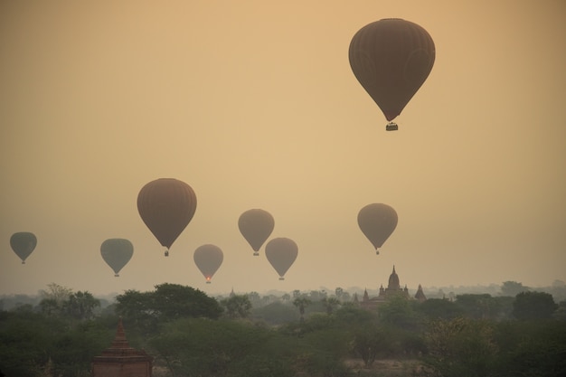 Sunrise with dusty smoke and many hot air balloons above The Bagan Archaeological Zone in 