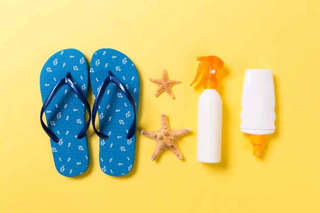 Sunscreen bottle or body spray on yellow background top view flat lay with copy space. Holiday vacation travel concept with beach sea accessories.