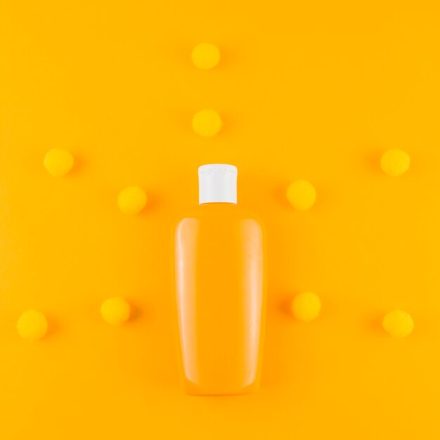 Sunscreen bottle with yarn pom pom ball on an orange backdrop
