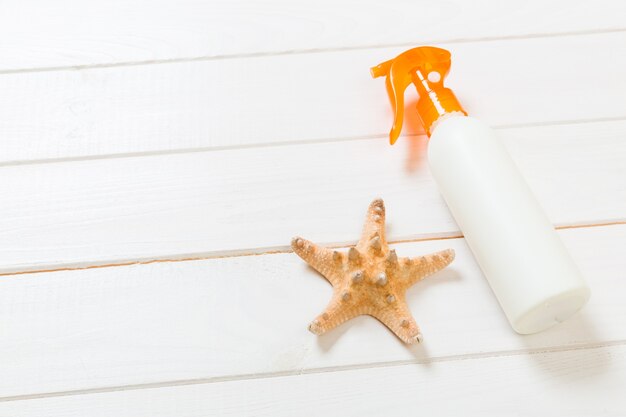 Sunscreen bottles with seashells on white wooden table. Travel healthcare accessories top view.