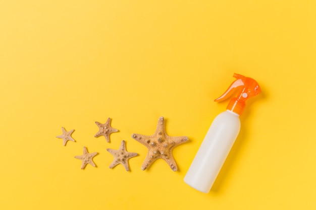 Sunscreen bottles with seashells on yellow table top view