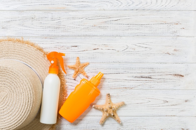 Sunscreen bottles with starfish and sunhat on white wooden table with copy space. Travel healthcare accessories top view.