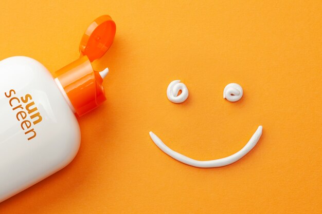 Sunscreen on orange background. Plastic bottle of sun protection and white cream in the shape of Smiley, smiling face.