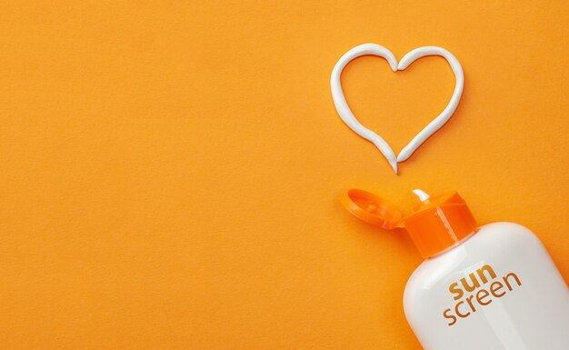 Sunscreen on orange background. Plastic bottle of sun protection and white heart-shaped cream.