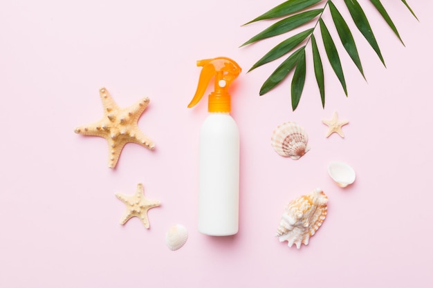 Sunscreen spray bottle Bottle with sun protection cream and sea shells with tropical green leaf on color background top view