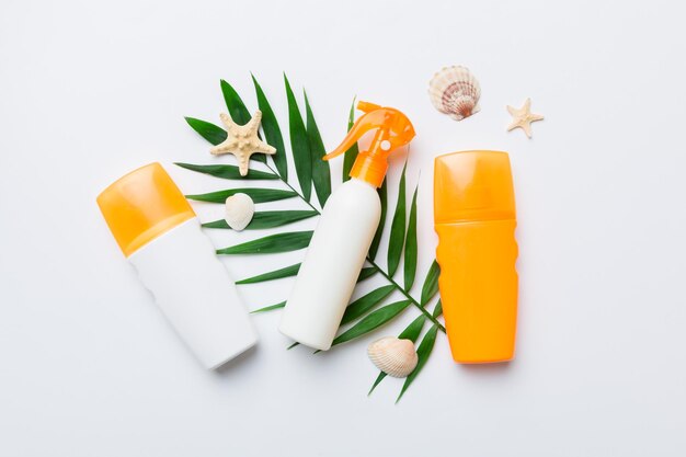 Sunscreen spray bottle Bottle with sun protection cream and sea shells with tropical green leaf on color background top view