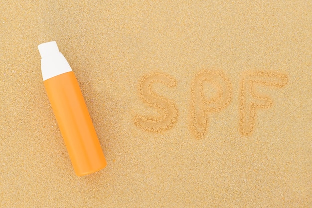 Sunscreen spray in orange bottle and inscription on the sand SPF