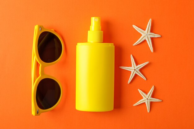 Photo sunscreen spray, starfishes and sunglasses on color background