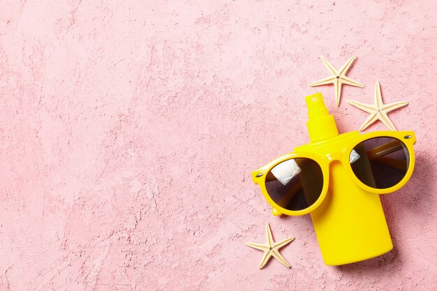 Sunscreen, sunglasses and starfishes on pink surface