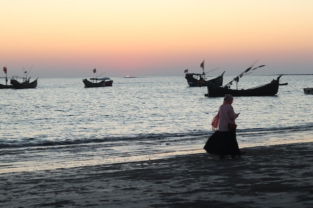 写真 夕日を歩く熱帯の海岸の若い女性の夕日