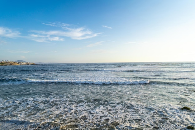 Sunset on the beach with blue sky and sea and white clouds.\
rock jetty. punta hermosa, lima.