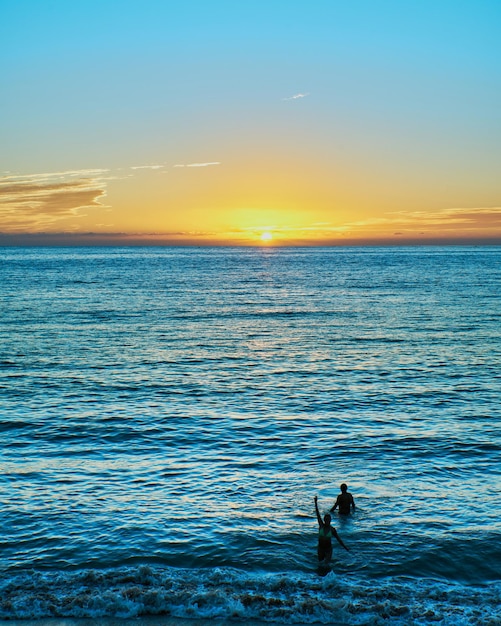 Foto tramonto sulla spiaggia con tramonto e una persona in bagno di mare