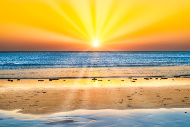 Sunset on beautiful sand beach with blue sea water and sun on sunset sky